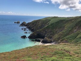 A coastal landscape with clear turquoise waters, rocky outcrops, and green hills.