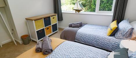 A bedroom with two beds, a window with a view of greenery, a bedside table, and a storage unit with multiple compartments.