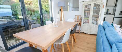 A dining area with a wooden table and chairs, a blue sofa, and a view of the outdoors through large windows.