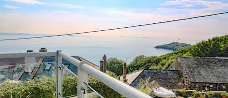 A balcony with a metal railing overlooking a coastal view, including a body of water and distant land.
