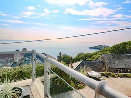 A balcony with a metal railing overlooking a coastal view, including a body of water and distant land.