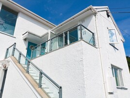 A white building with a staircase leading to a balcony with glass railings.