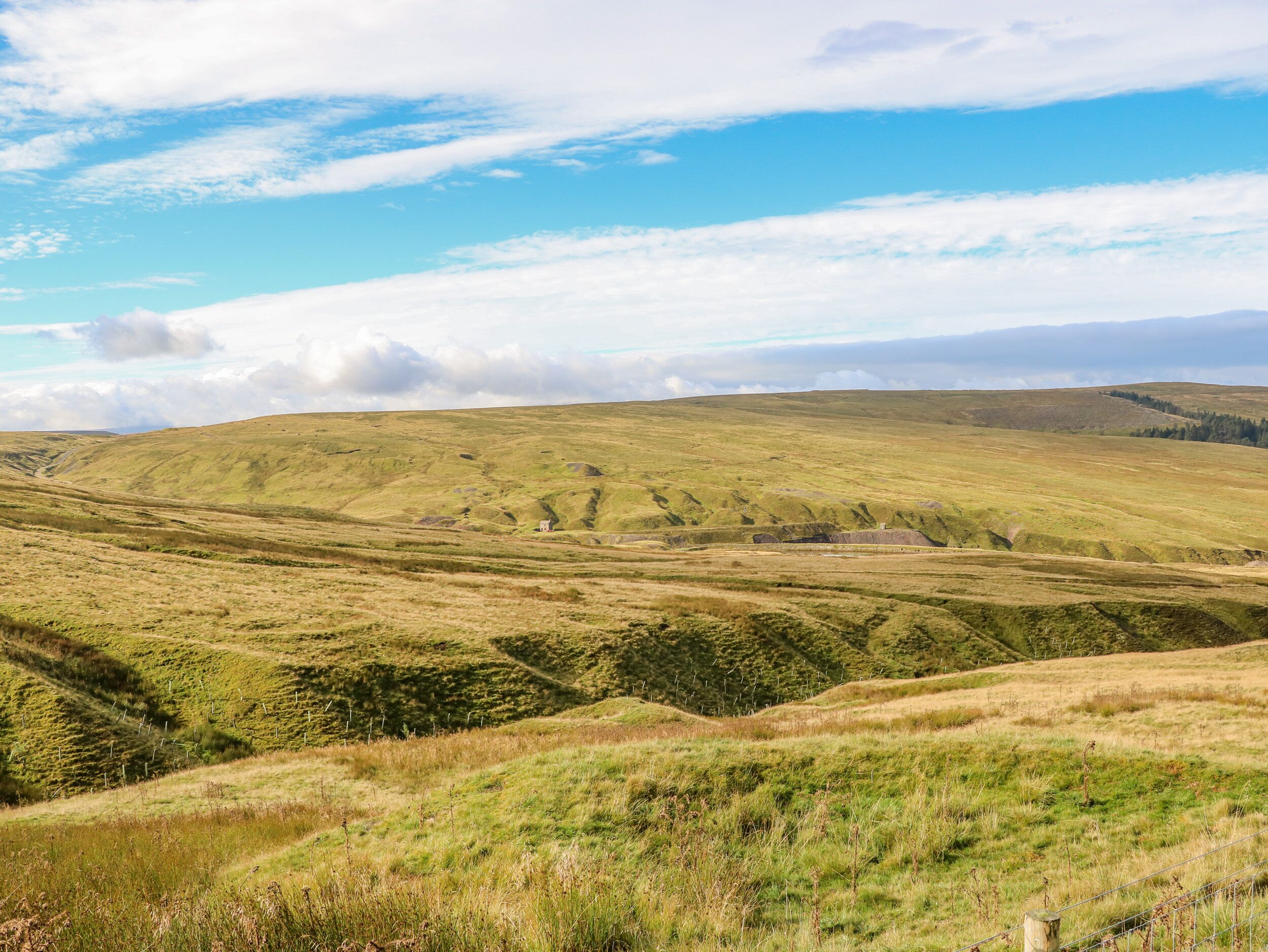Une vue panoramique d’un paysage vallonné, avec une petite maison nichée au milieu des collines.