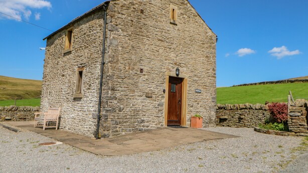 Un bâtiment en pierre avec une porte en bois et une petite fenêtre, un banc et une pancarte sur laquelle on peut lire « Field House ».
