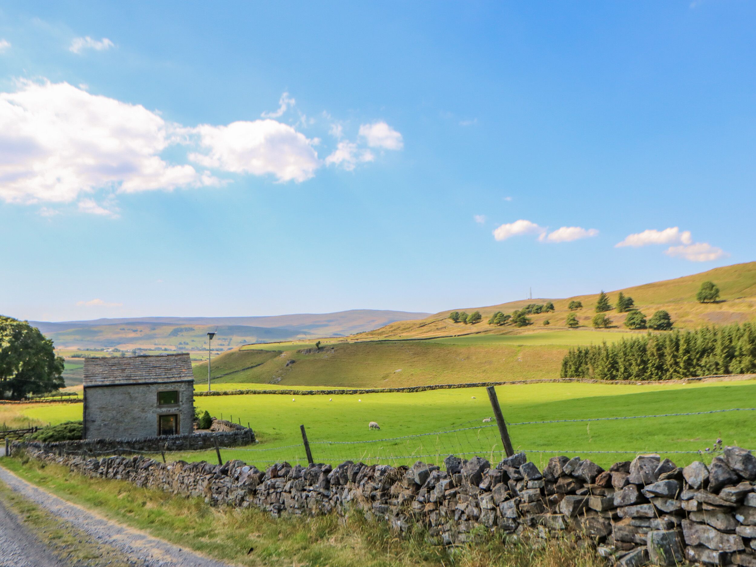 A rural landscape with a stone wall, a small stone building, and green fields.