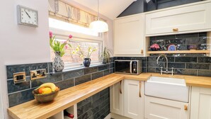 A modern kitchen with a wooden countertop, a built-in microwave, a sink, and a window with plants. - 4 Ford Street (Durham)