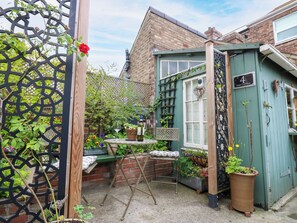 Ein kleiner, umzäunter Garten mit Tisch, Stühlen und Topfpflanzen.