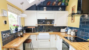 A compact kitchen with white cabinets, a microwave, a sink, and a toaster. There are wooden shelves with decorative items and a window with a view of greenery. - 4 Ford Street (Durham)