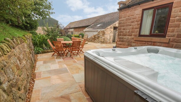 A hot tub in a stone patio area with a wooden table and chairs.