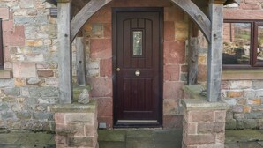 A stone building with a dark wooden door, a stone staircase, and a wooden porch with a triangular roof.
