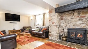 A cozy living room with leather sofas, a wooden coffee table, a stone fireplace, and a flat-screen TV mounted on the wall.