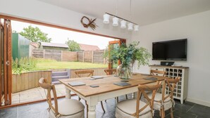 A dining area with a wooden table and chairs, a vase with greenery, a television, and a wine rack. - Griff Lodge (York)