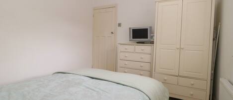 Un dormitorio con cama, armario y televisor sobre un aparador.