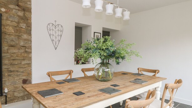 A dining area with a wooden table, six chairs, a vase with greenery, and a heart-shaped wall decoration. - Griff Lodge (York)