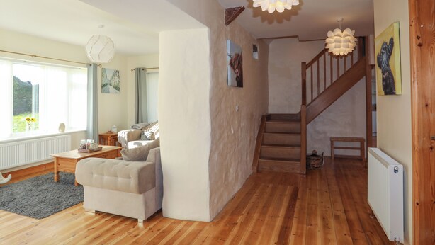 Un salon spacieux doté d’un plancher en bois, d’un canapé blanc, d’un escalier en bois et d’une grande fenêtre avec des rideaux.