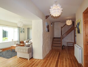 A spacious living room with a wooden floor, a white sofa, a wooden staircase, and a large window with curtains. - Nant y Gof (Holyhead)