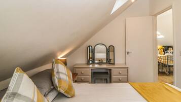 A bedroom with a sloped ceiling, a bed with a white and yellow checkered bedspread, a bedside table with a mirror, and a dresser.