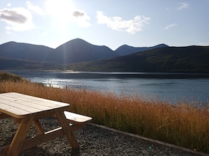 A wooden picnic table by a lake with mountains in the background.