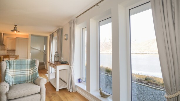 Ein Zimmer mit großem Fenster, einem Sessel, einem kleinen Tisch und Blick auf ein Gewässer.