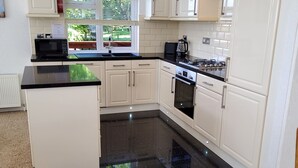 A modern kitchen with white cabinets, a black countertop, a built-in oven, and a window with blinds. - Lodge 11 (Tavistock)