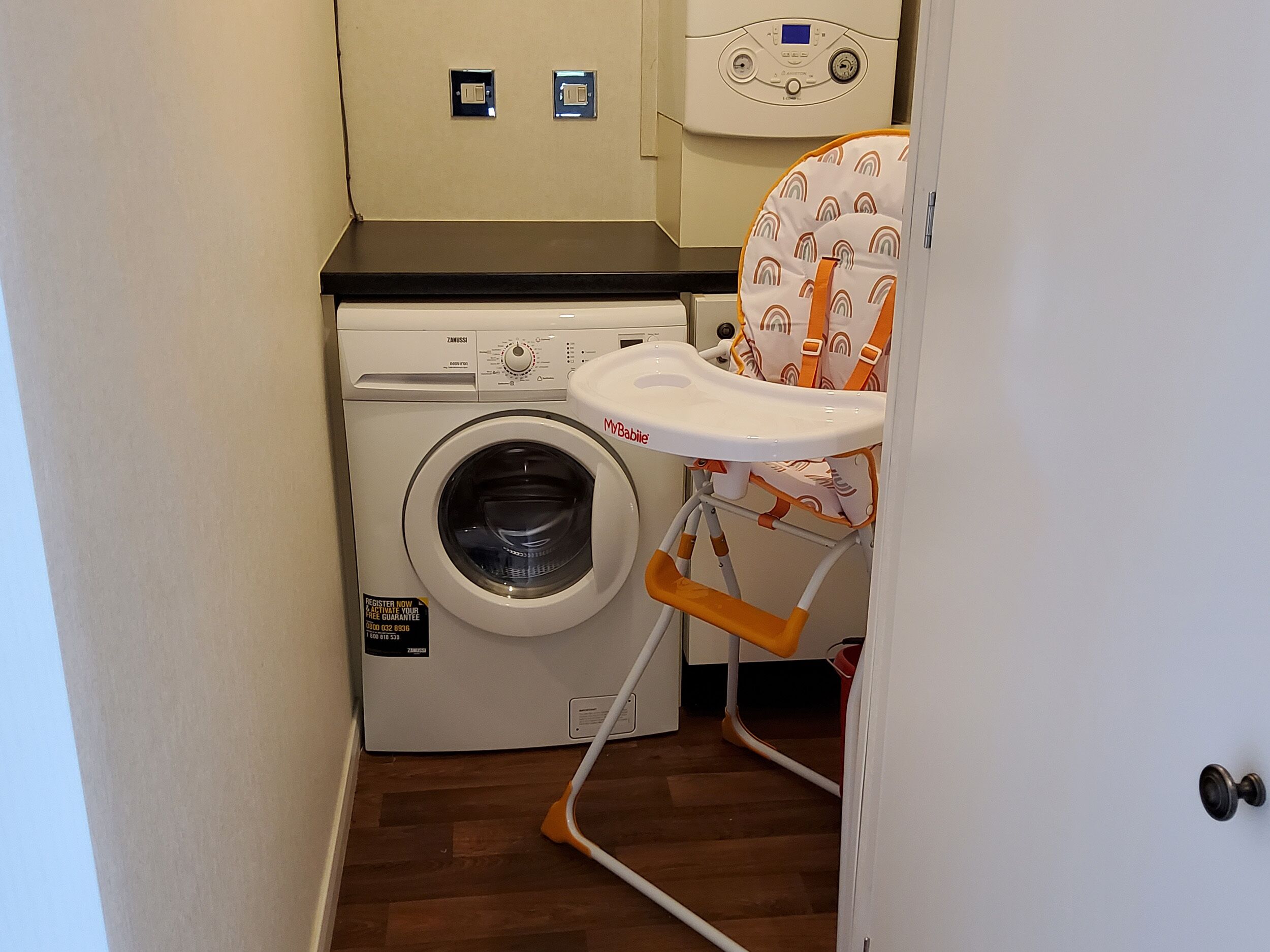 Un área de lavandería compacta con una lavadora de carga frontal y una pequeña silla con asiento de la marca MyBaby.
