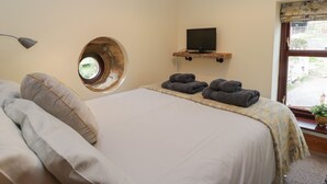 A bedroom with a bed, a round window, a mounted TV, and towels on the bed.
