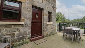 A stone building with a wooden door, windows, and a small outdoor seating area with a table and chairs.