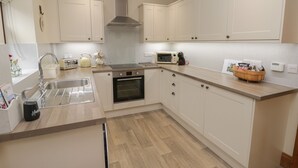 A modern kitchen with white cabinets, a stainless steel range hood, a built-in oven, a microwave, and a wooden countertop.