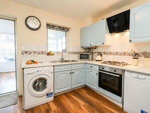 A compact kitchen with white appliances, a microwave, a sink, and a stove.