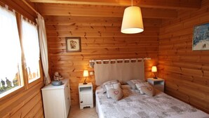 Een houten slaapkamer met een bed, twee nachtkastjes, een hanglamp, een ingelijst beeld en een raam met gordijnen.