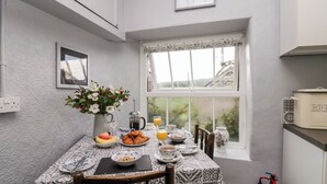 Une table de petit-déjeuner dressée avec des croissants, des fruits et du jus d’orange, une cafetière et un vase de fleurs.