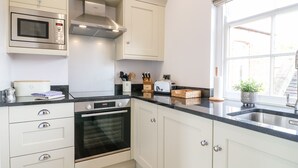 A modern kitchen with white cabinetry, a built-in microwave, an oven, and a window with a view of the outside. - Dovedale (Ashbourne)