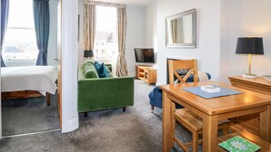A hotel room with a bed, a green sofa, a wooden dining table, a TV, and a lamp. - Dovedale (Ashbourne)