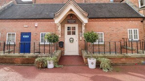 A traditional brick building with a central entrance, a blue door, and two potted plants on either side. - Dovedale (Ashbourne)