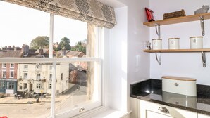 A kitchen with a window overlooking a street, wooden shelves with jars, and a black countertop.