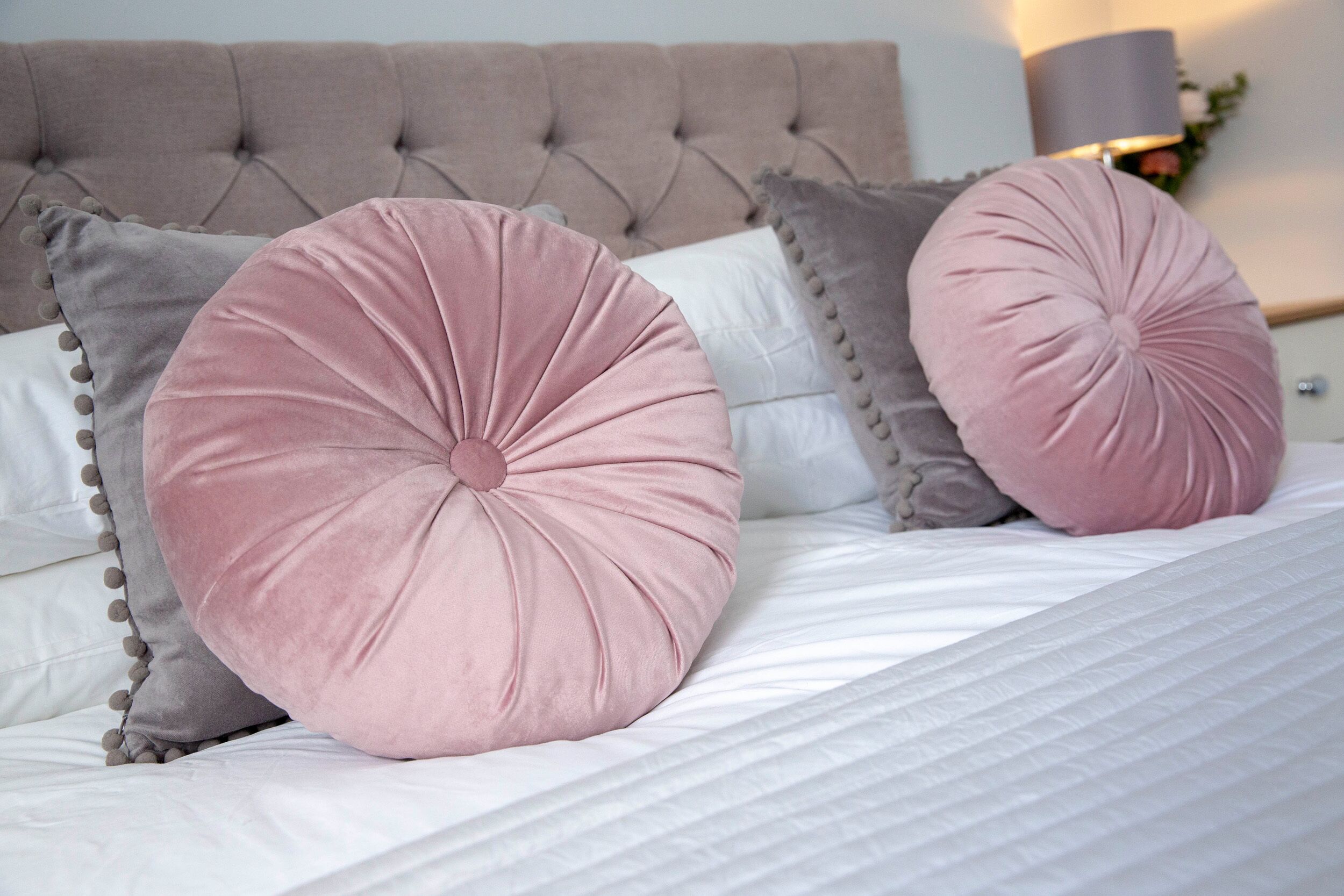 A bed with a tufted headboard, two large round pillows, and a white comforter.