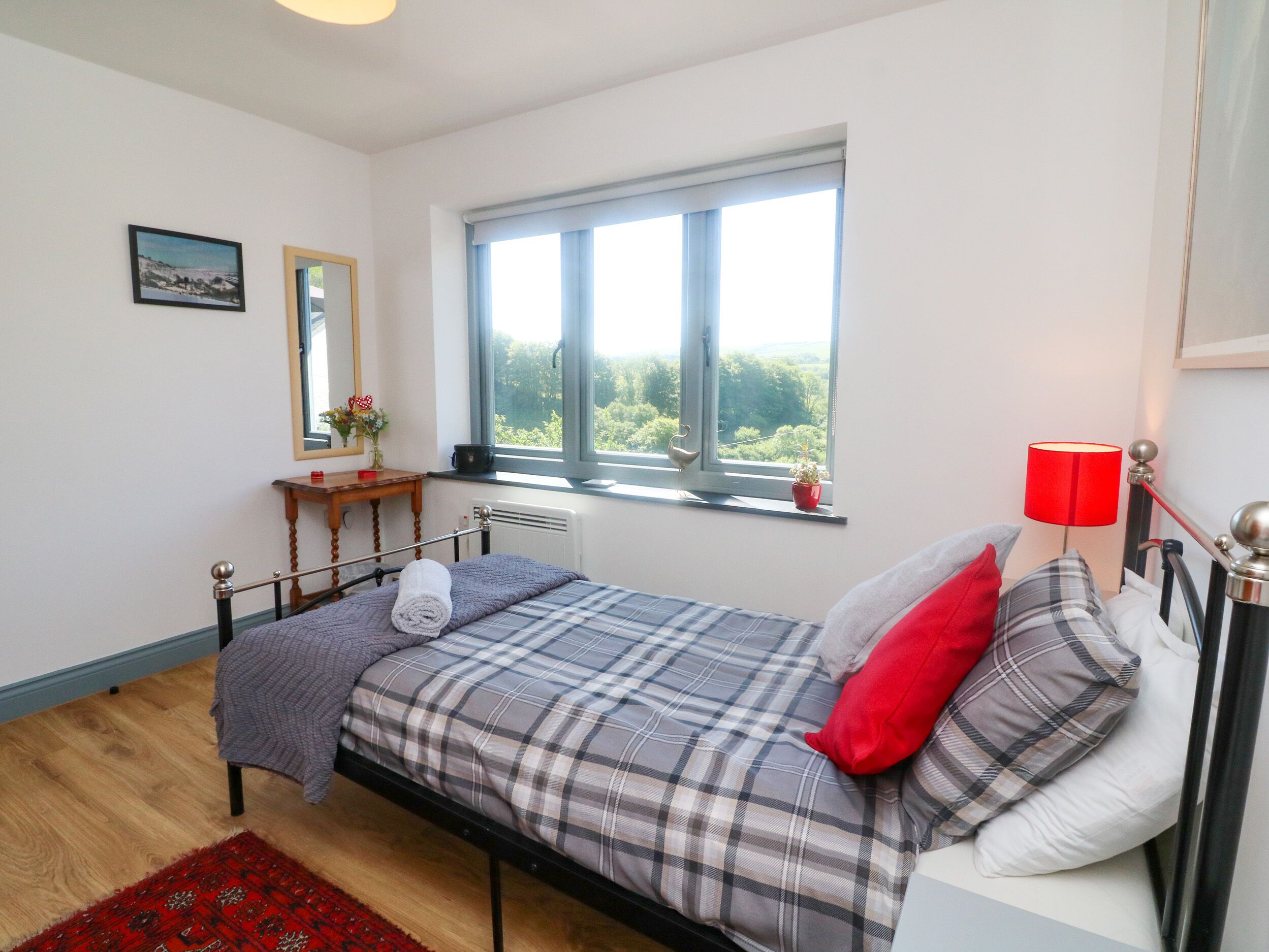 A bedroom with a bed, a window with a view, a bedside table, and a red lamp.