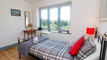 A bedroom with a bed, a window with a view, a bedside table, and a red lamp.