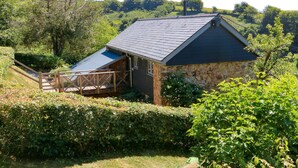 A stone building with a sloped roof, a wooden deck, and a view of a lush green landscape. - Higher Bumsley Barn (Barnstaple)