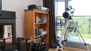 A cozy living room with a bookshelf, a telescope, and a fireplace. - Higher Bumsley Barn (Barnstaple)