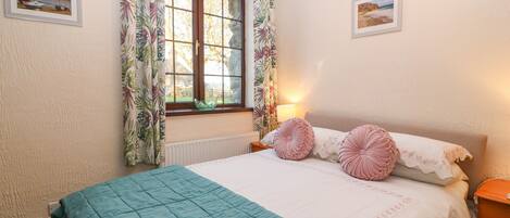 A bedroom with a bed, a window with curtains, a bedside lamp, and two framed pictures on the wall.