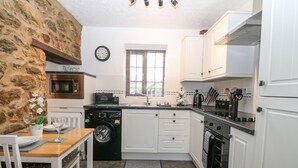 Cozinha compacta com armários brancos, máquina de lavar, relógio e área de refeições com uma mesa posta para dois.