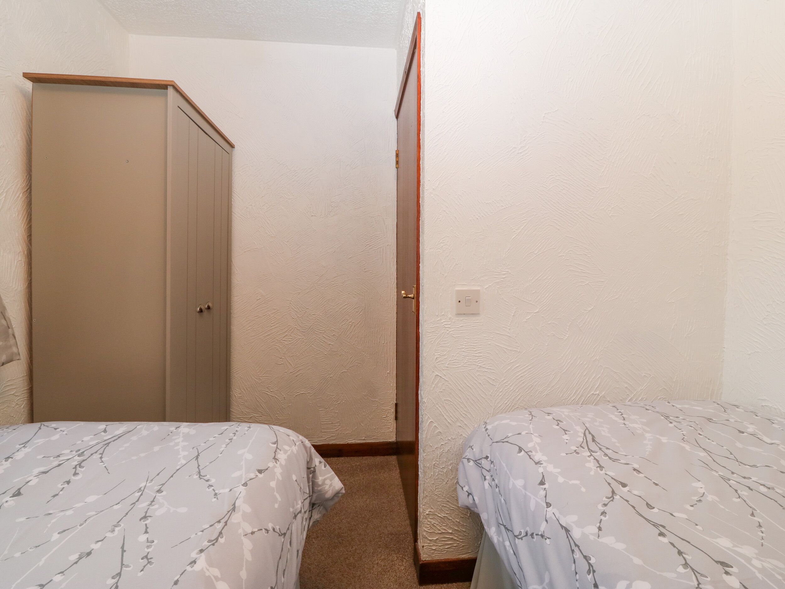 Pequeña habitación con dos camas individuales, un armario y una puerta que da a otra estancia.