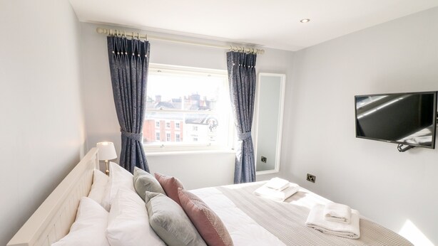 A hotel room with a bed, a TV, a window with curtains, and a view of buildings outside. - Manifold Dale (Ashbourne)