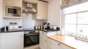 A modern kitchen with white cabinetry, a built-in microwave, a stainless steel range hood, a toaster, and an oven. - Manifold Dale (Ashbourne)