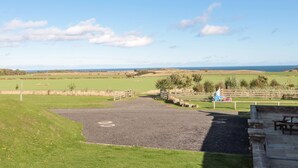 A rural landscape with a gravel area, picnic tables, and a view of the sea. - Stable D'or (Alnwick)