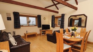 A cozy living room with a brown leather sofa, a wooden dining table with chairs, a television, and a window with curtains. - Stable D'or (Alnwick)