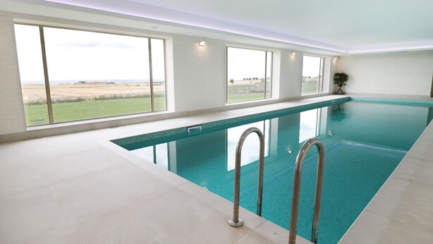 Ein großer, überdachter Pool mit freiem Blick auf die umliegende Landschaft durch große Fenster.