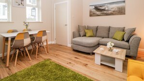 A modern living room with a grey sofa, a wooden coffee table, and a dining area with a white table and chairs. - Cove Cottage (Torquay)