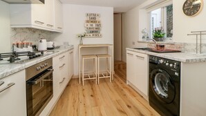A modern kitchen with white cabinets, a stainless steel range, a built-in oven, a dishwasher, and a wooden floor. - Cove Cottage (Torquay)